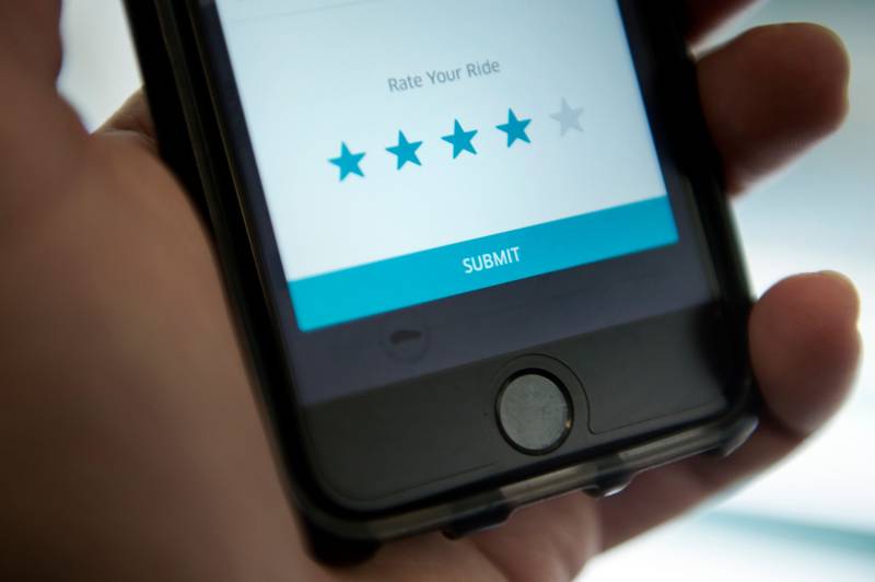 A hand holds up a smart phone that shows a screen for rating Uber drivers