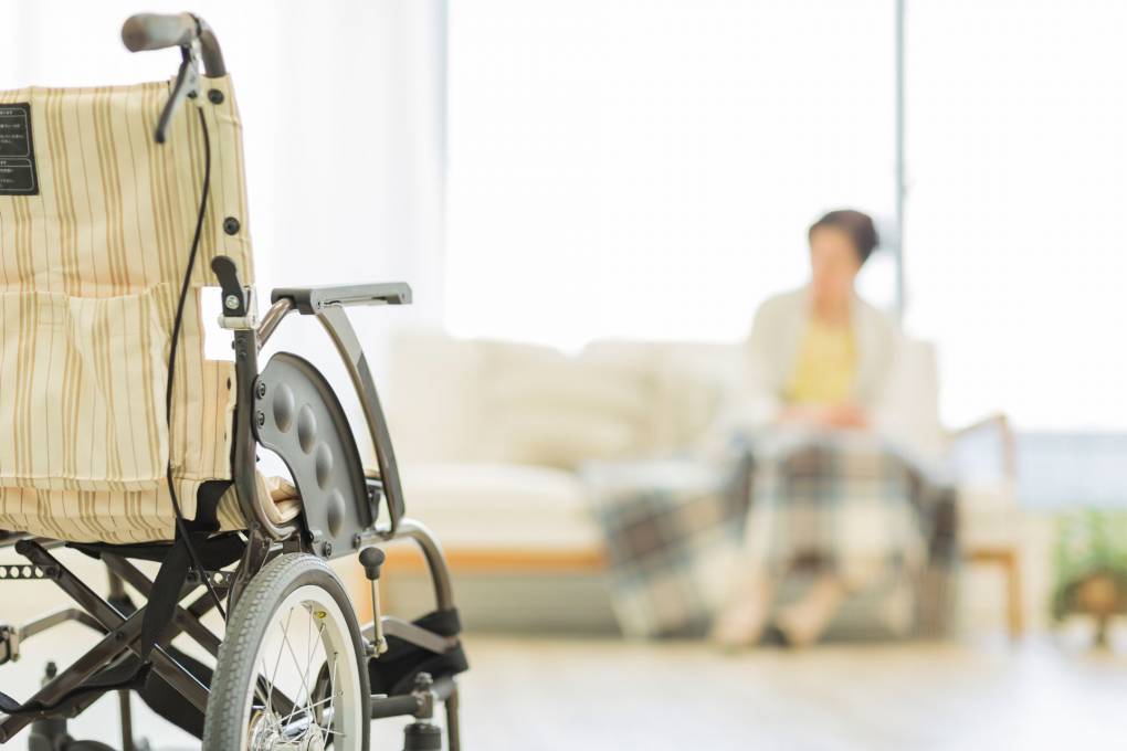 empty wheelchair in foreground, blurry nursing home resident in background