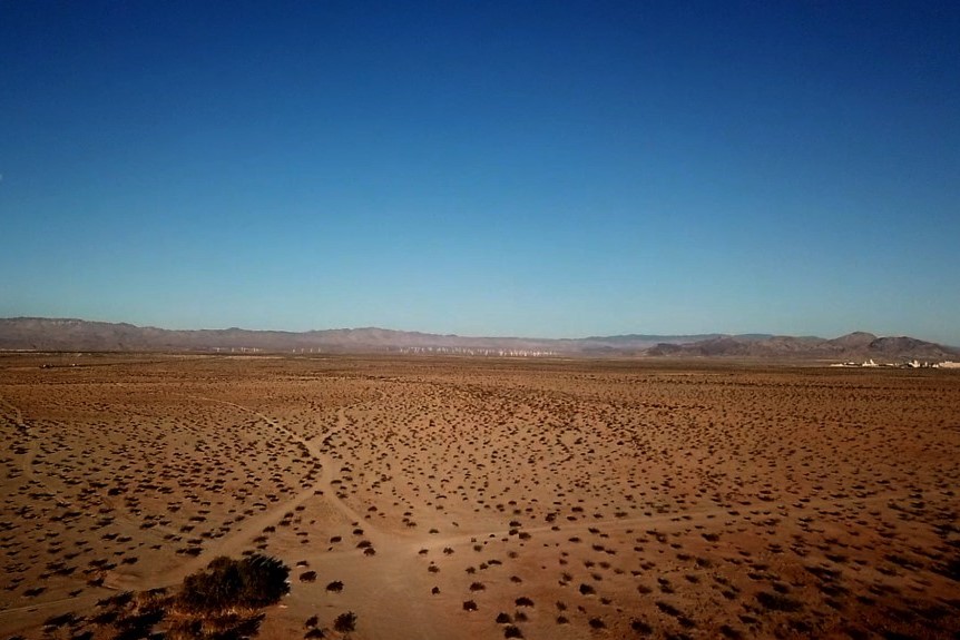 An aerial view of a desert in Imperial Valley. A few bushes are surrounded by vast stretches of dry land.