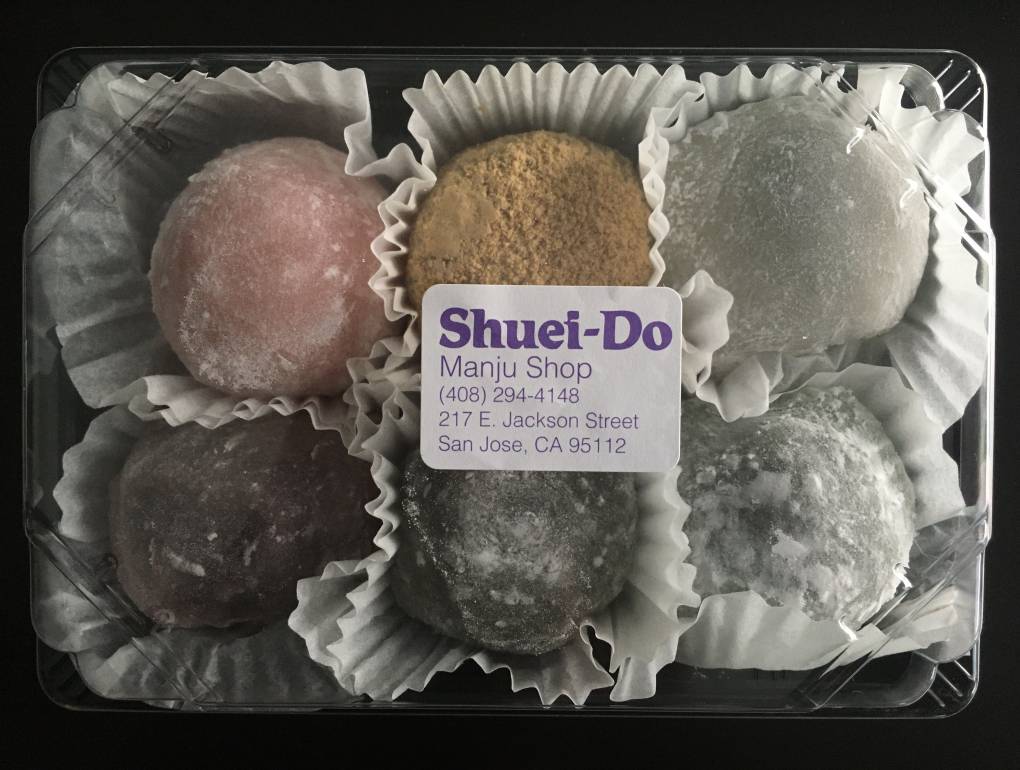 A box of six colorful mochi, with a plastic top and the shop's label on it.
