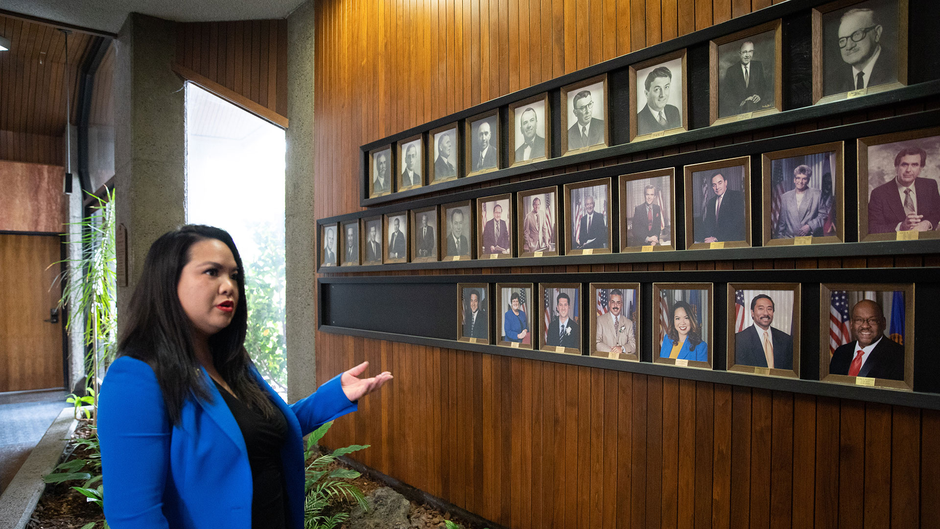 Daly City Mayor Juslyn Manalo points to a wall of past mayors on the wall of City Hall. For many years white men dominated, but more recently the city's diverse community is represented here too.