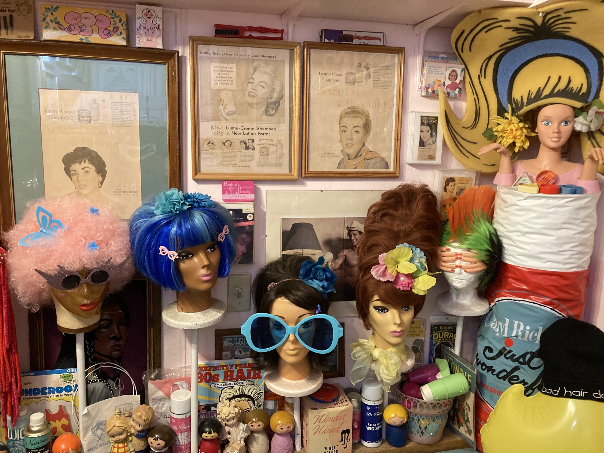 Multi-colored wigs adorn mannequin heads with vintage posters in the background. 