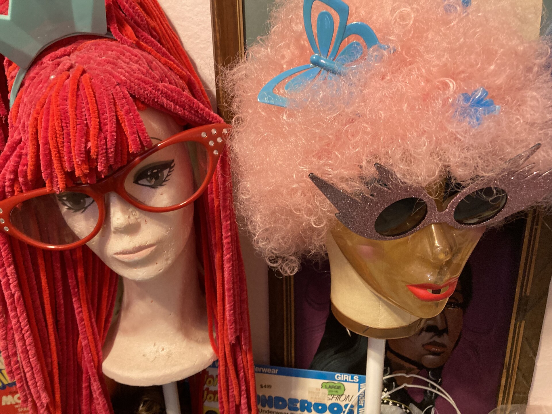 Two mannequin heads sit with a red raggedy-anne wig and a pink curly-haired wig.