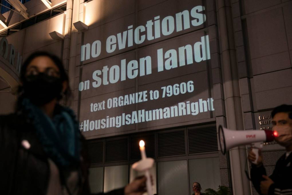Protesters hold candles in front of a projection that says, "no evictions on stolen land."