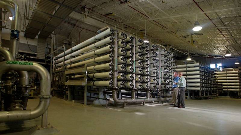 Two workers looking at a series of pipes inside a desalination plant.