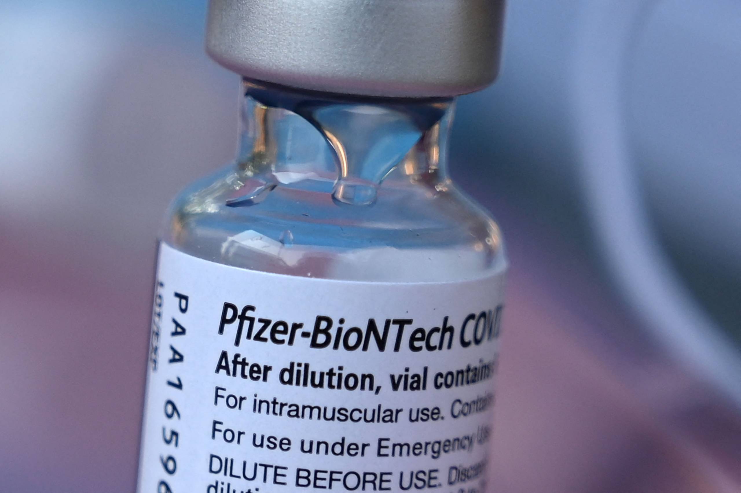A close-up of the label on a small glass vial, with a silver-colored cap, of the Pfizer-BioNTech vaccine.