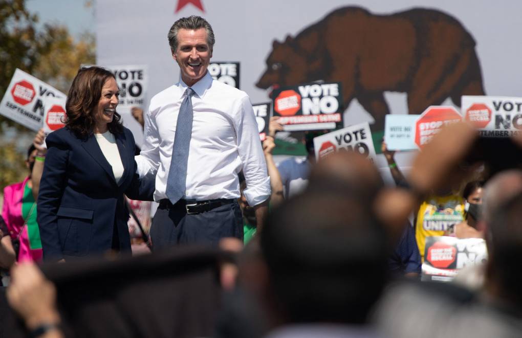 VP Kamala Harris and Governor Gavin Newsom stand together smiling in front of a crowd.