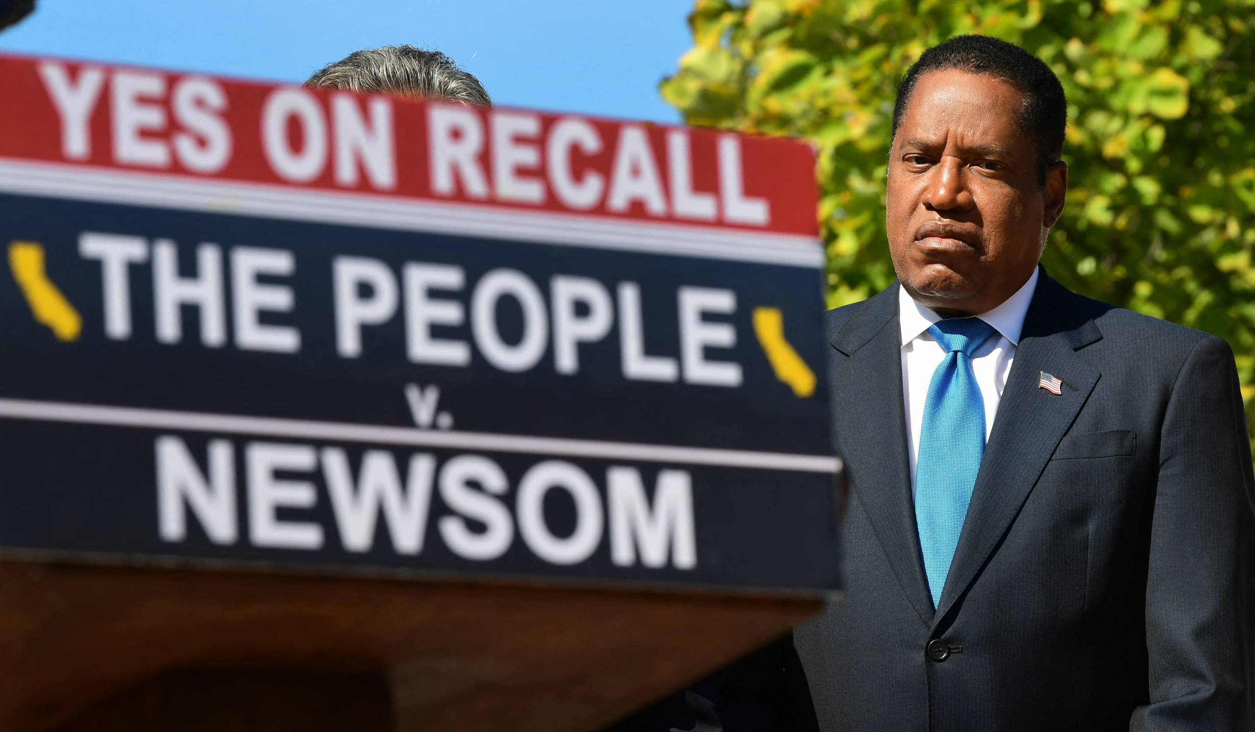 Larry Elder stands near a podium sign that reads, "Yes on Recall, The People v. Newsom."