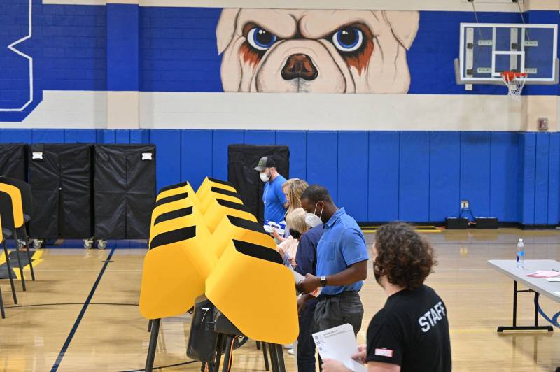 A group of about 5 voters fill out their ballots in booths that have been set up in a gym.