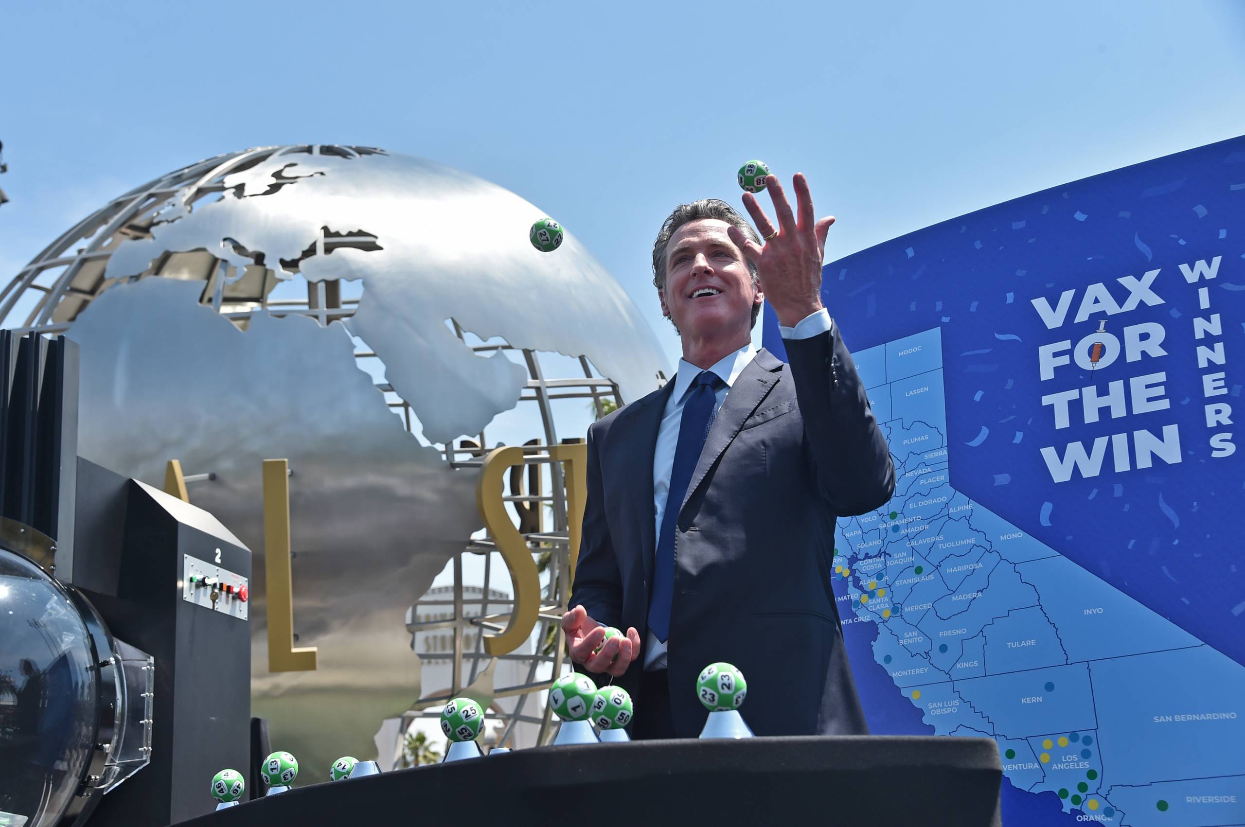 Gov. Newsom throws a few small lottery balls into the air in front of the Universal Studios globe statue.
