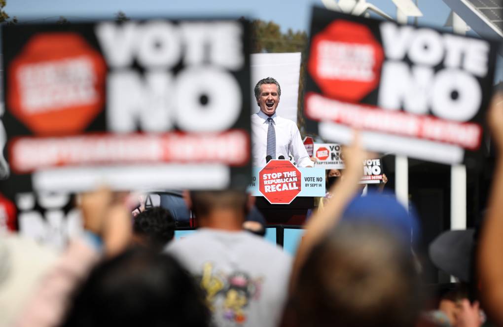 Gov. Gavin Newsom speaks to a crowd, with many holding "Vote No" signs.