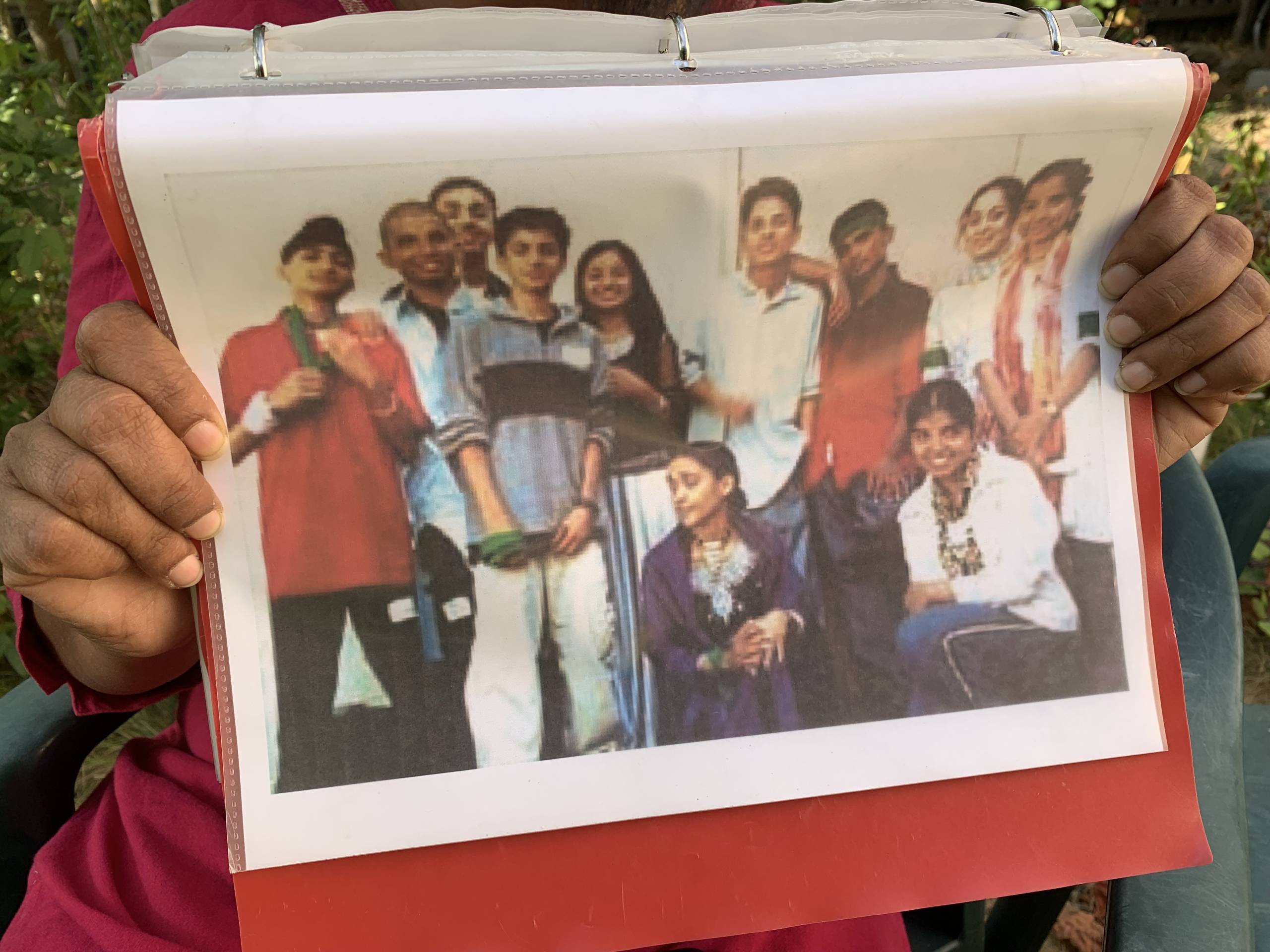 Two hands hold up a picture in a binder of a group of smiling teenagers.