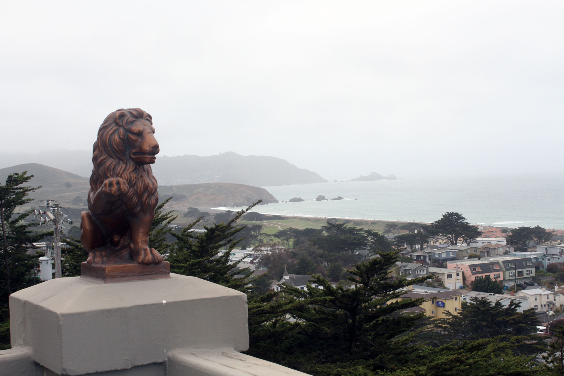 A lion statue in the foreground with view of Pacific ocean behind.