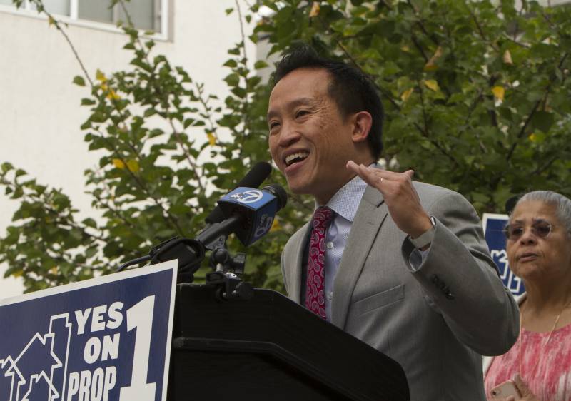 David Chiu, in a suit and tie, gestures as he speaks into a microphone at a podium.