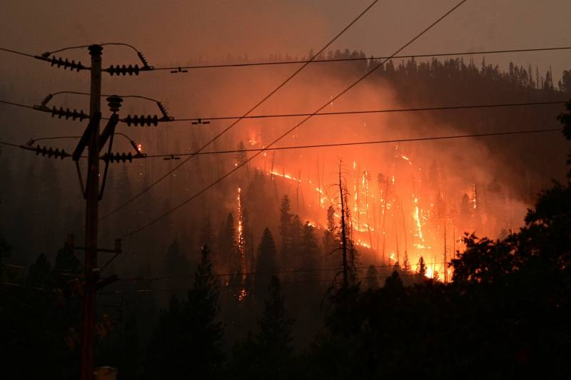 A silhouette of power lines in the foreground is backlit by a hillside on fire.