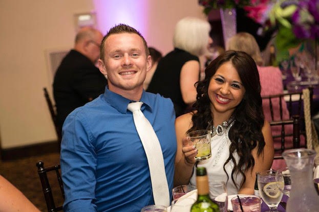 A smiling couple in formal dress sit together at a table at a party.