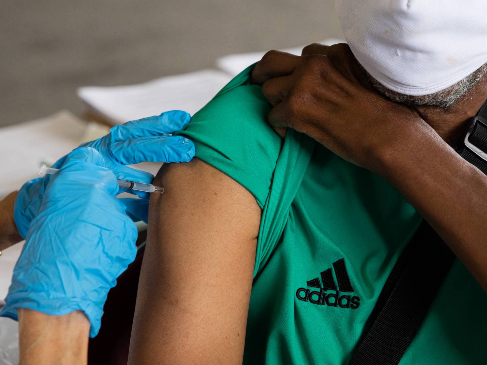 Blue-gloved hands give a vaccine in one shoulder.