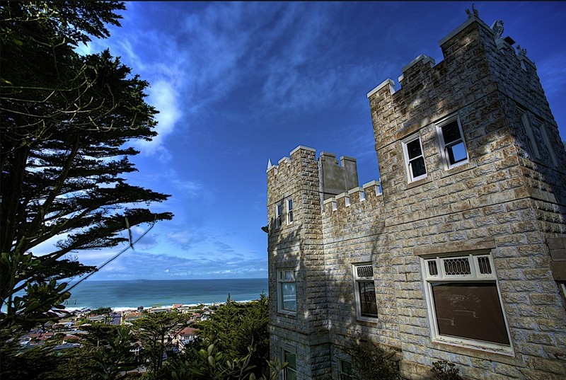 A blue sky and ocean behind a castle like building.