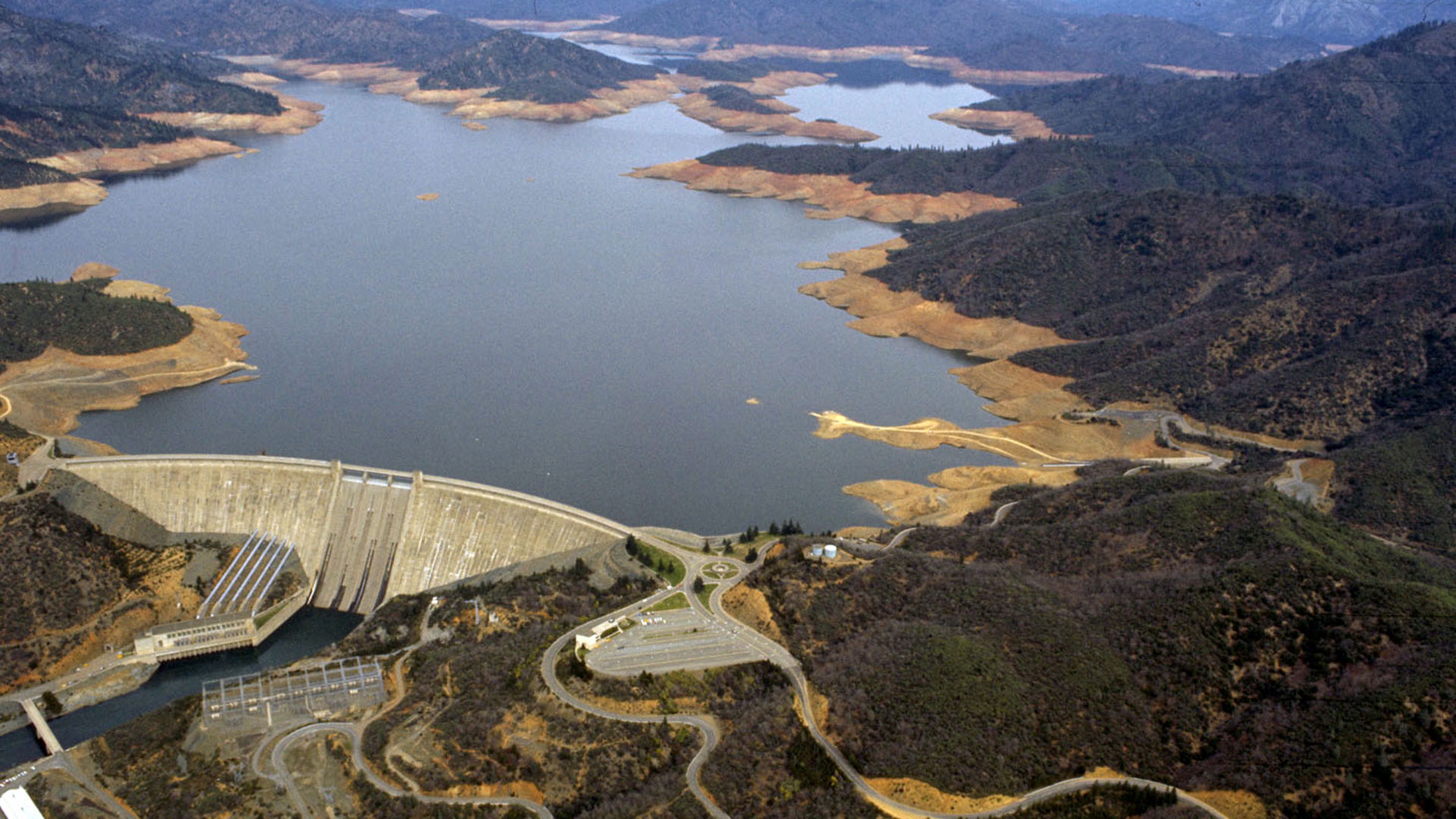 Aerial view of a lake. The dam is visible and a dry shoreline peeks out above the water.