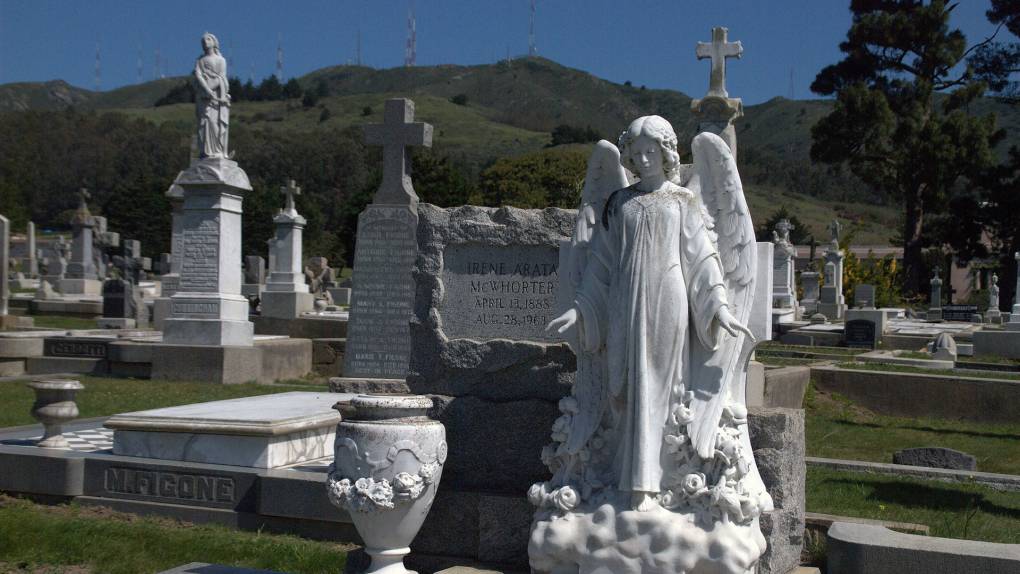 A stone statue of an angel in the foreground with many gravestones behind it.