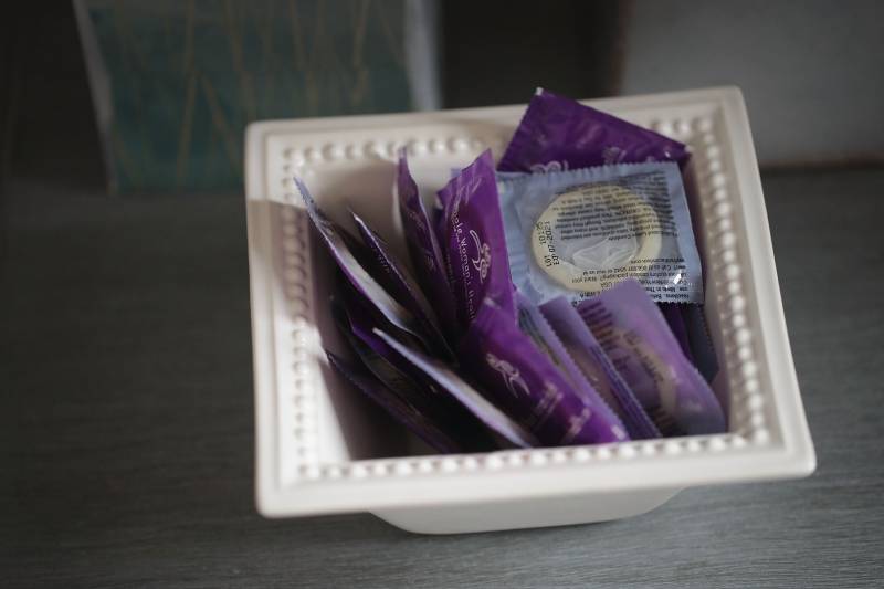 A white clay bowl sits on a table, full of condoms in purple wrappers.