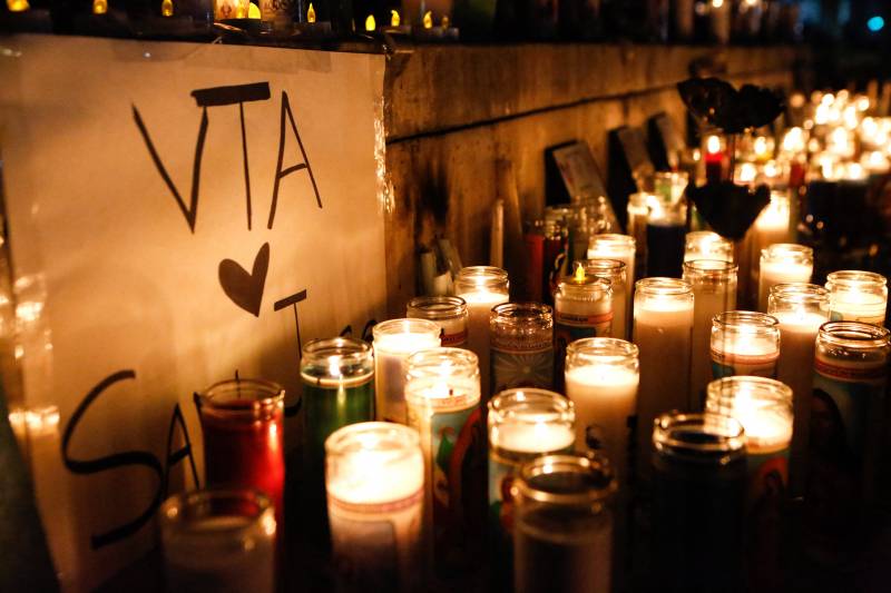 A nighttime shot of dozens of glassed-in candles lining a low wall alongside a sign that reads, "VTA [heart] San Jose."