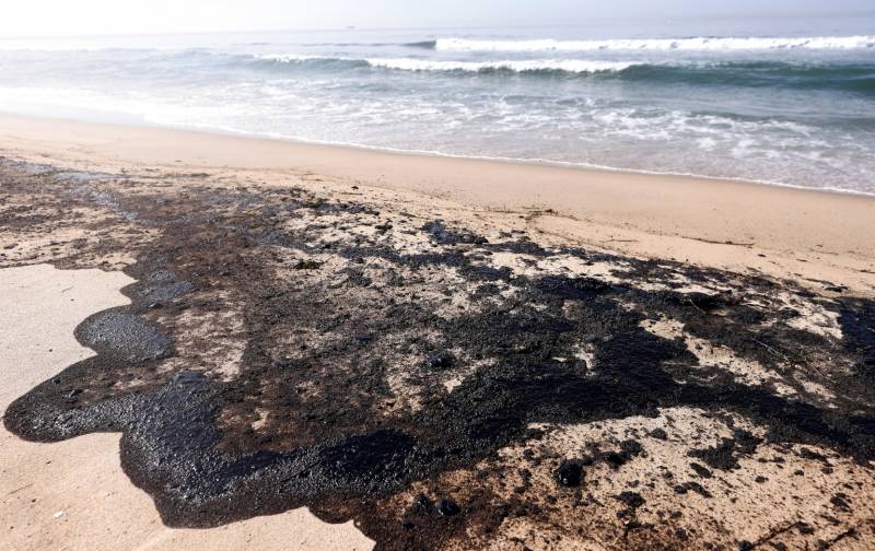 A giant black pool of oil washes up on a beach. Waves are seen in the background.