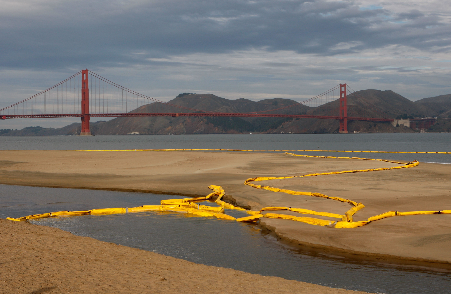 Long yellow inflatables, called booms, are coiled in the water and beach inside the Golden Gate Bridge.