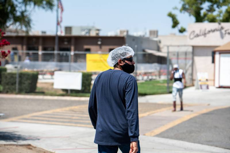 A man wearing a plastic hair net and a long-sleeved shirt walks along a sidewalk toward a long, low industrial building.