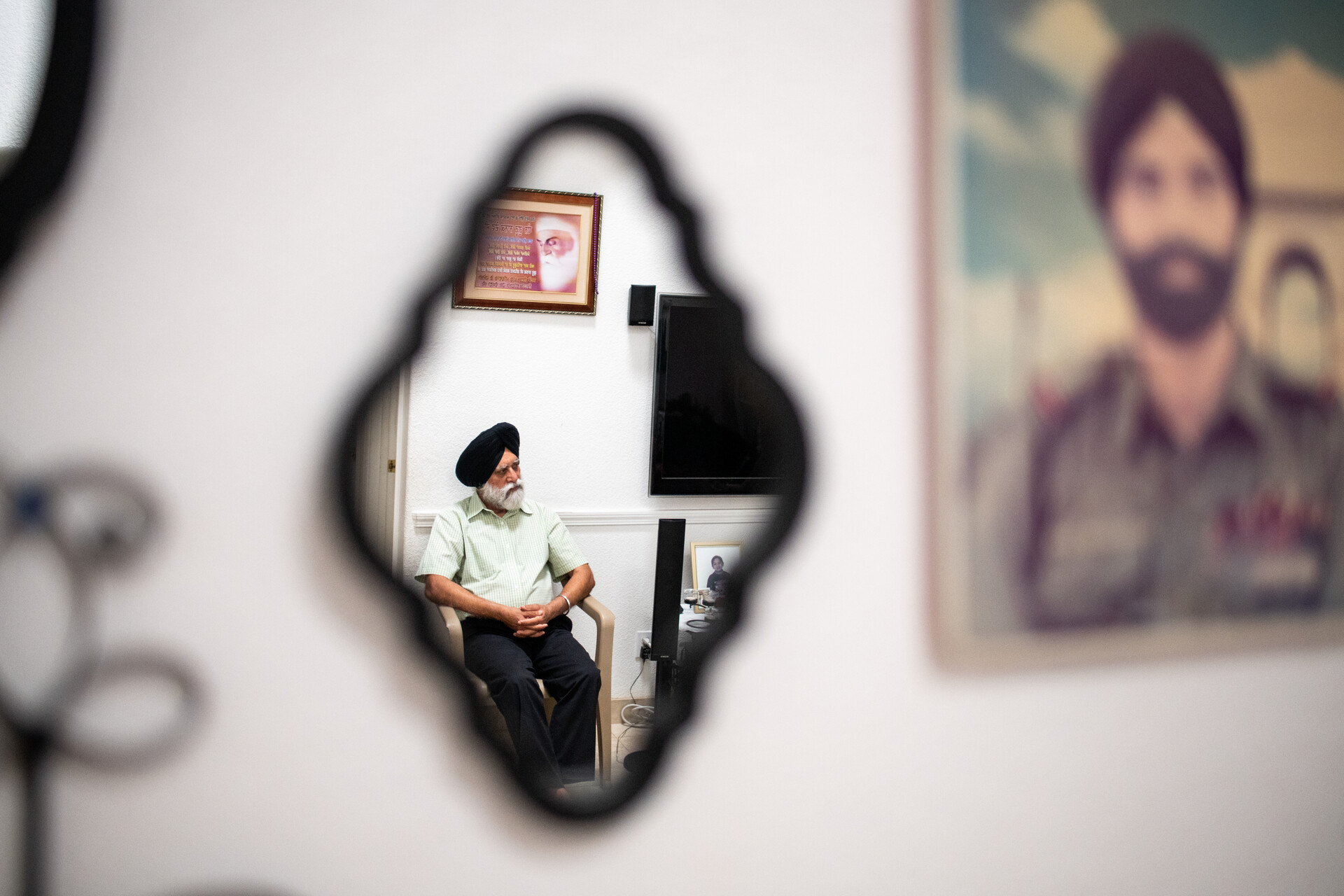 Mr. Singh is reflected in a mirror on a wall; the wall a poster with an image of a bearded man with a turban are in soft focus.