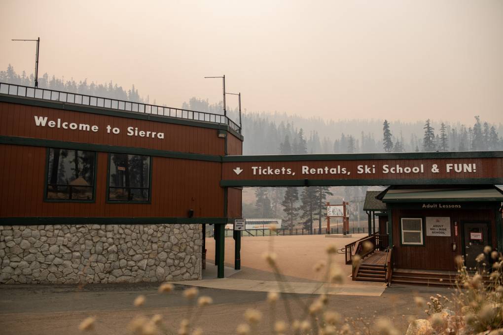 The front gates of a resort stand in front of a mountainous landscape covered in orange and gray smoke.