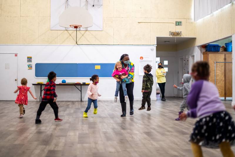 Bri Davis leads a game for a classroom of preschool children in a gym.