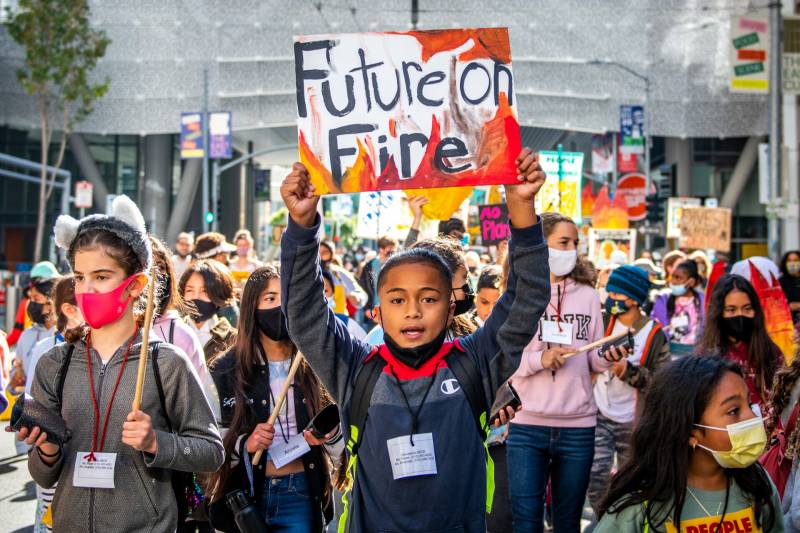 A young man walks through a crowd of students with a hand-made sign that reads "Future on Fire"