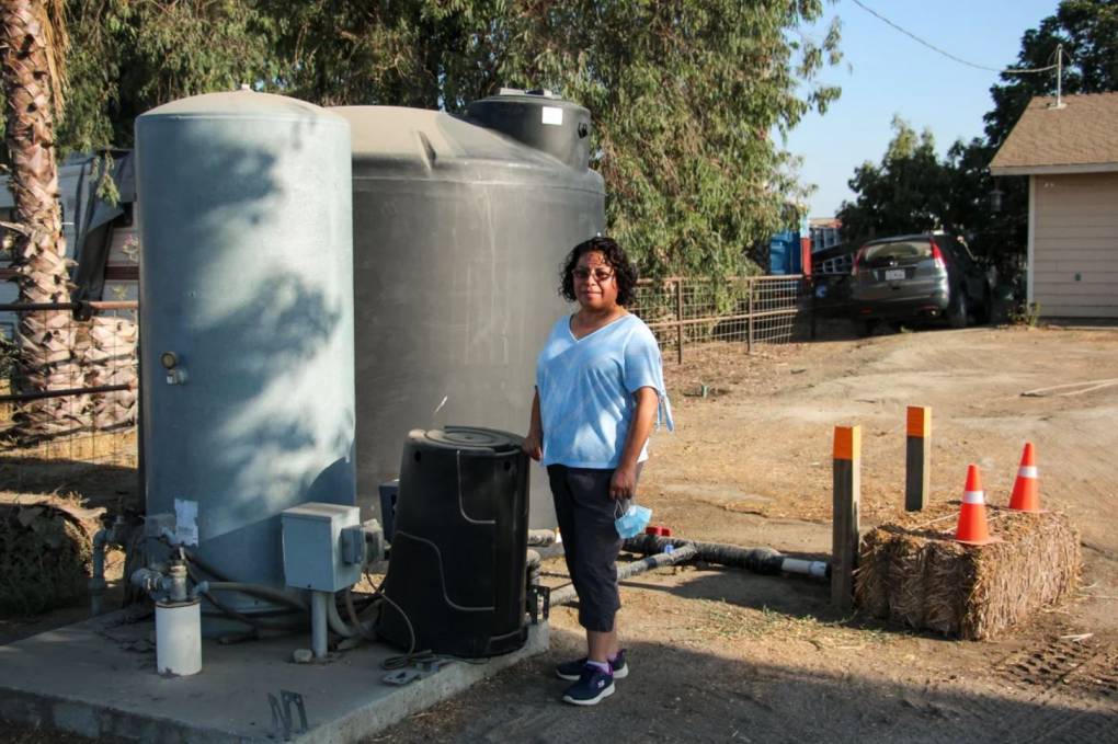 Esther Espinoza stands outside next to a very large tank of water, which sits above the well.