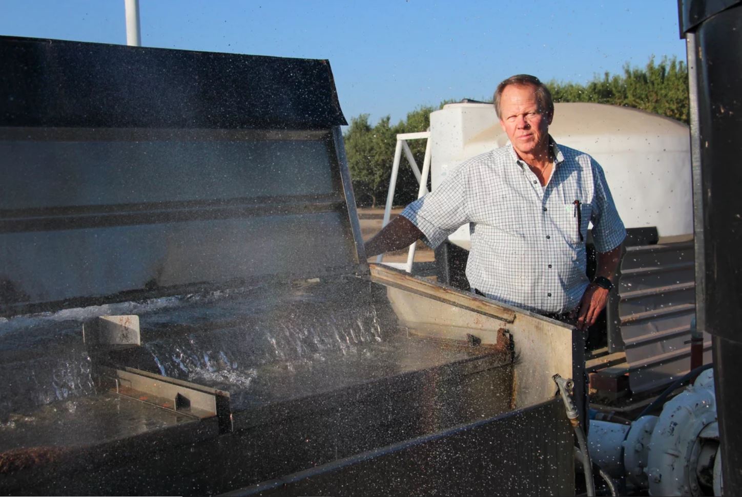 Rick Cosyns stands next to his farm's well, a large metal container with water flowing inside.