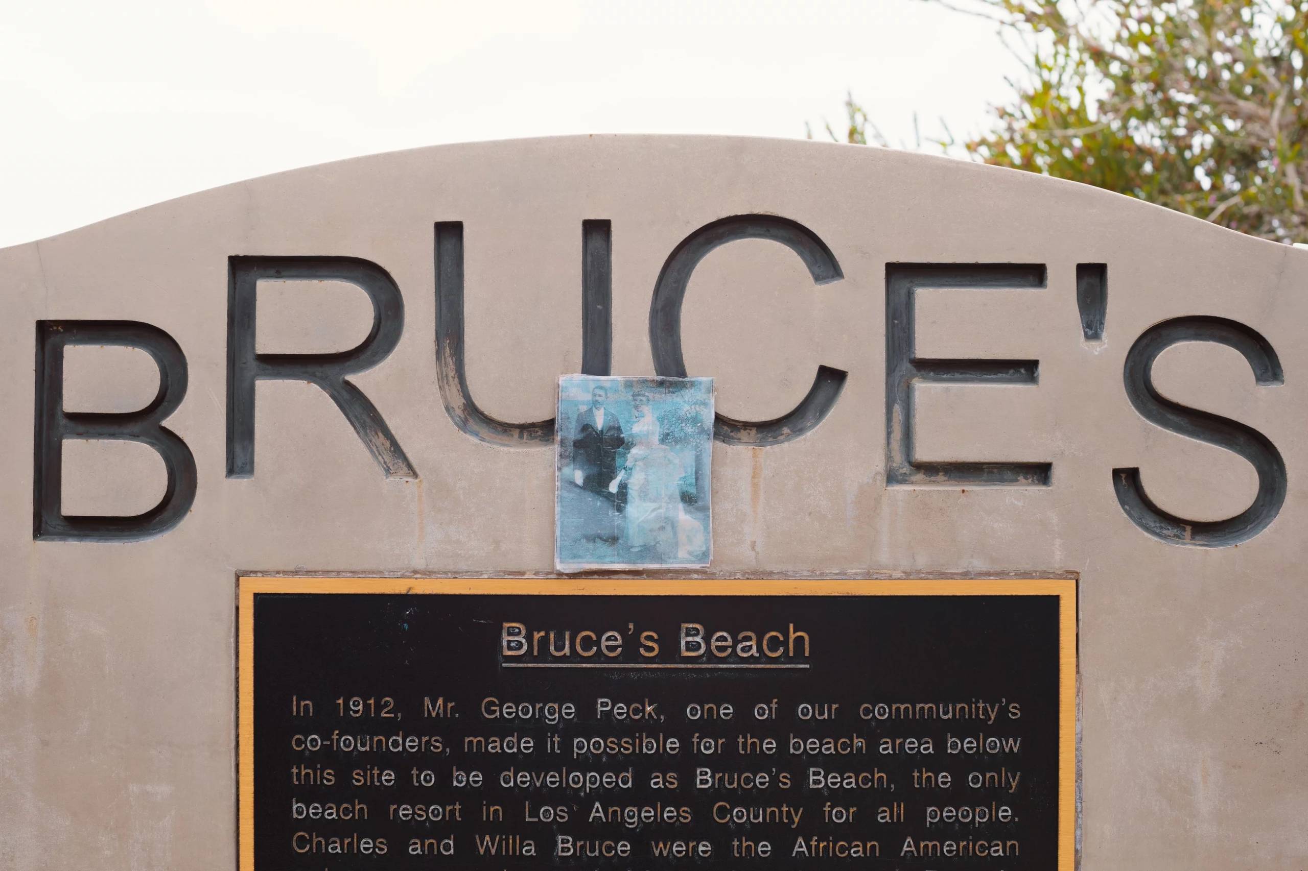 A monument saying "Bruce's" with a plaque engraved on it, with a laminated photograph propped on the plaque.