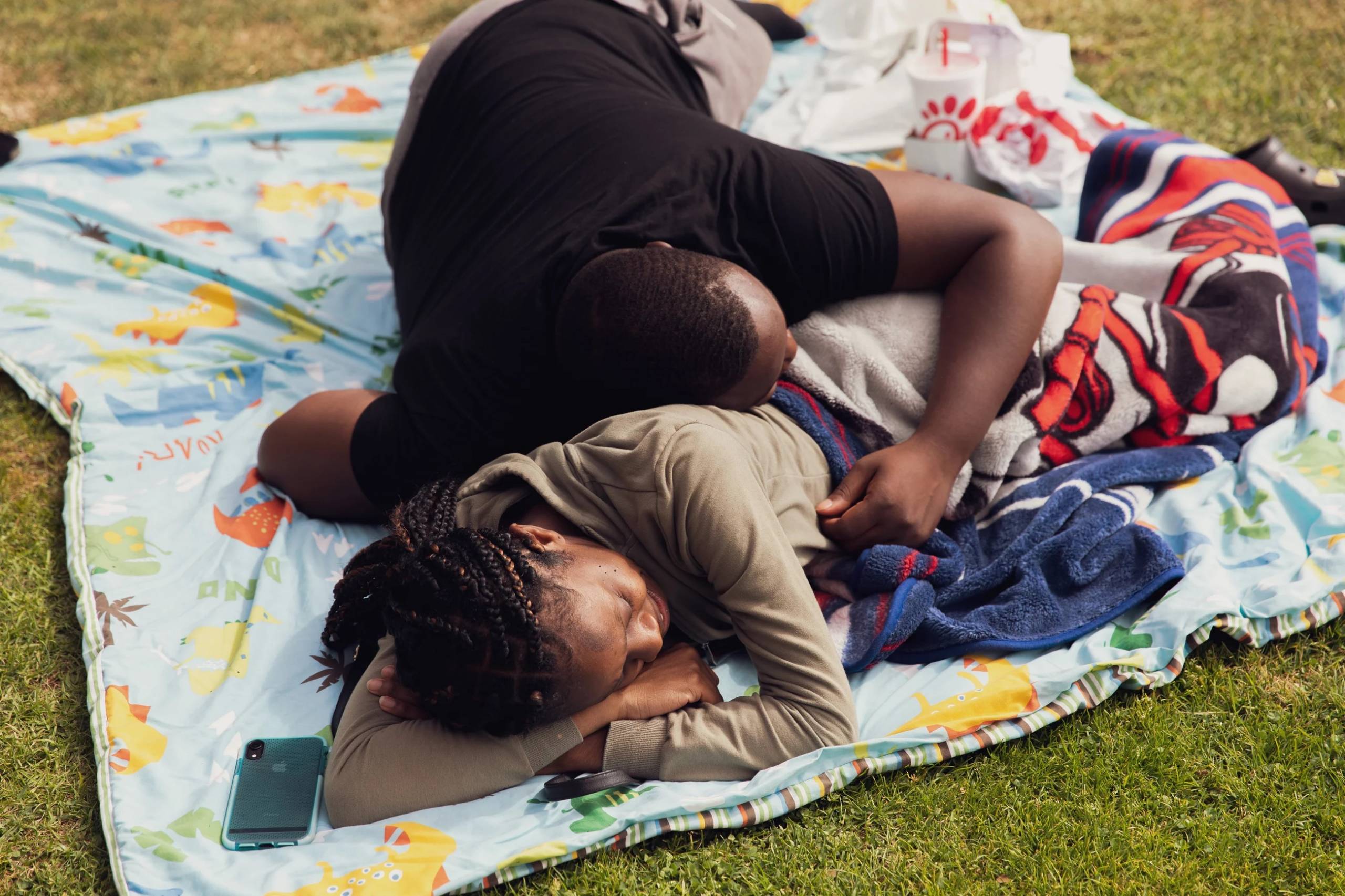 A couple cuddles on a fuzzy blanket on the grass.