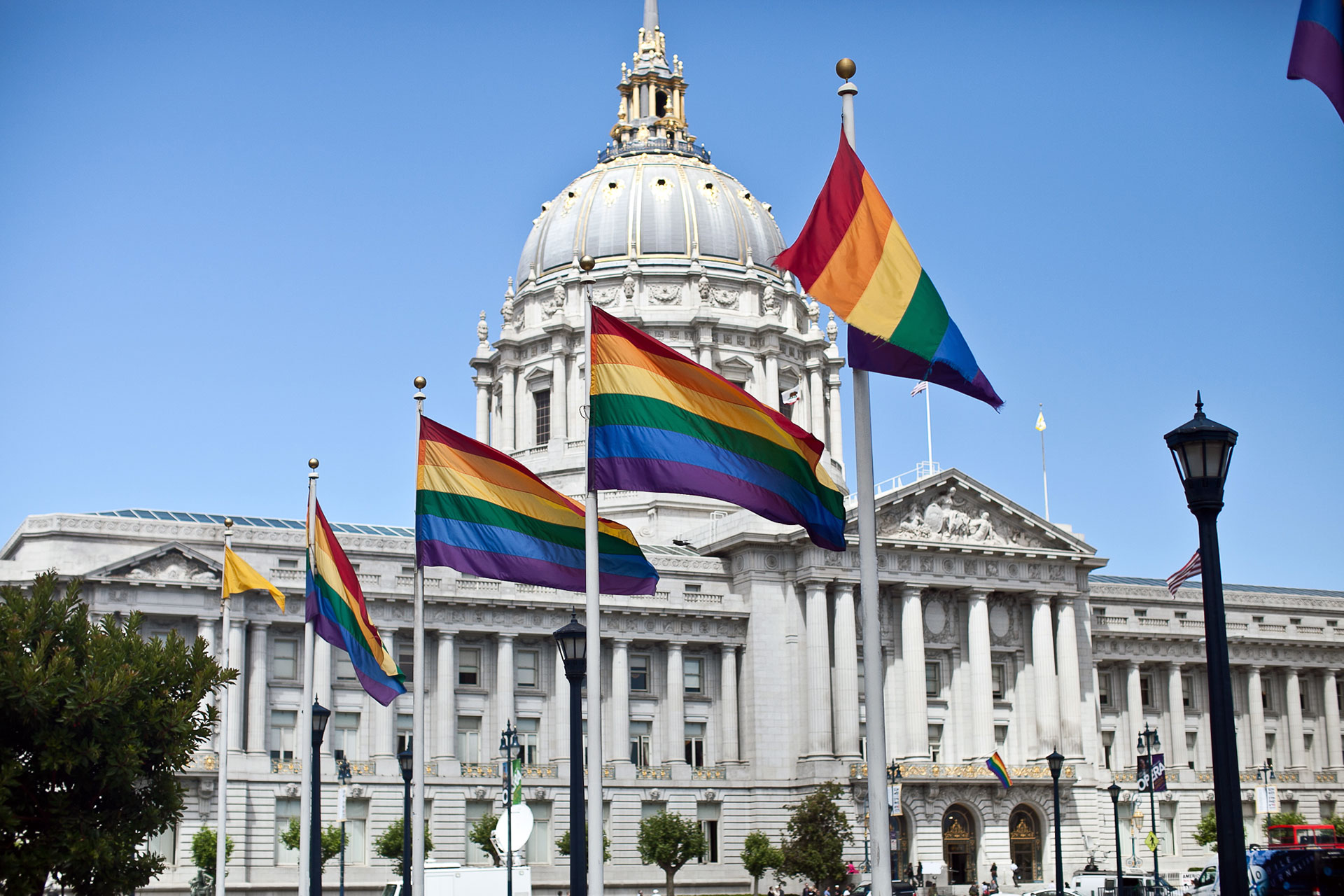 Rainbow flags fly in front of an impressive white stone building with a dome.