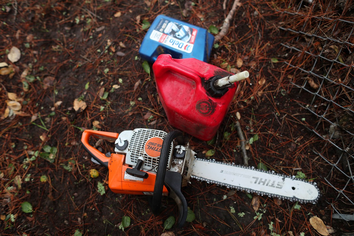 A chain saw lies on the ground, next to a red gasoline tank.