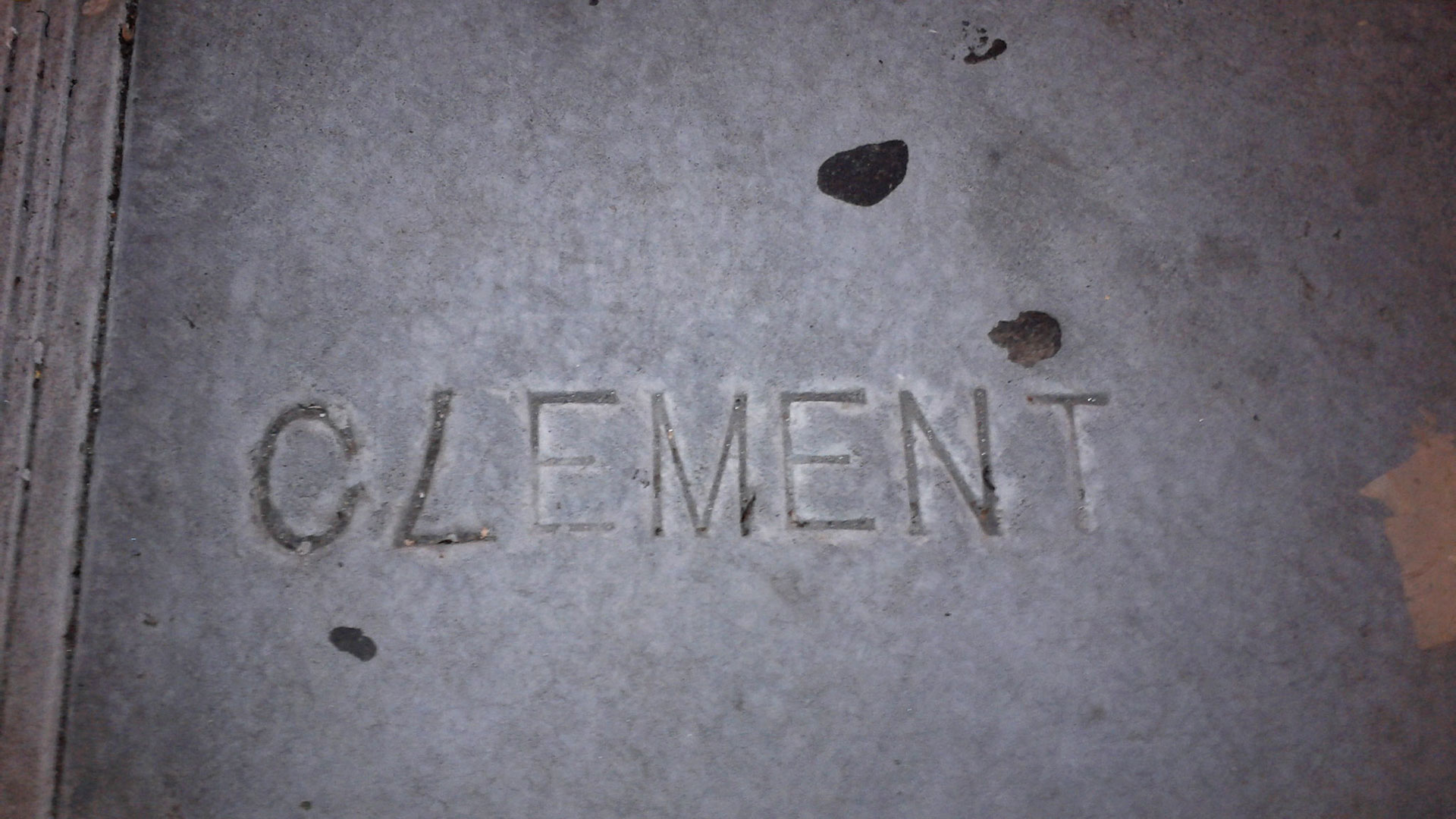The name Clement is stamped into a sidewalk with an upside down 7 as an L.
