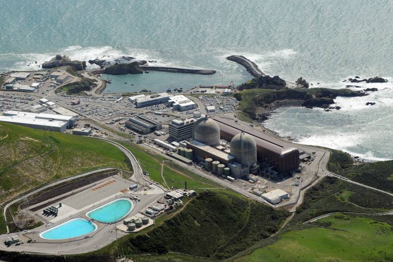 An aerial shot of the nuclear plant, which contains two large silos, various buildings, a large parking lot and vats of water, all located a few yards off the beach.