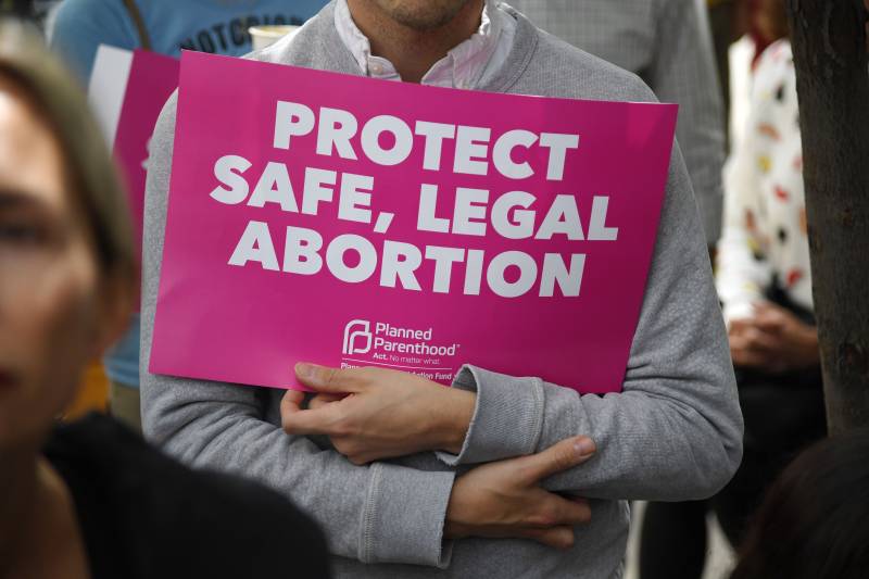 A person holds a sign that says 'PROTECT SAFE, LEGAL ABORTIONS'