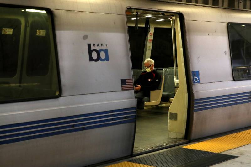 The BART passenger wears a facemask and is the only passenger visible within the train.