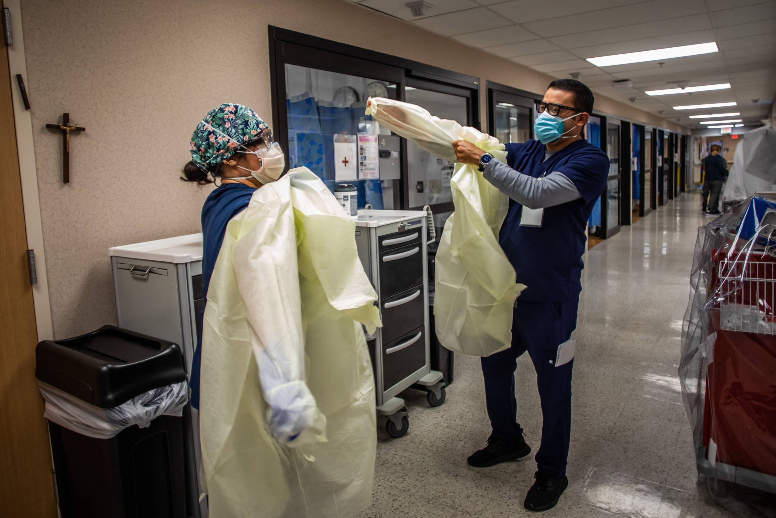 The nurses stand in a hospital hallway and put their scrubs on and other protective gear.