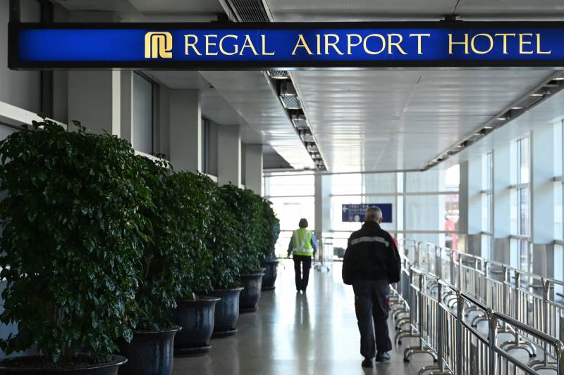 A long hallway in an airport. A sign hangs above and reads, "Regal Airport Hotel."