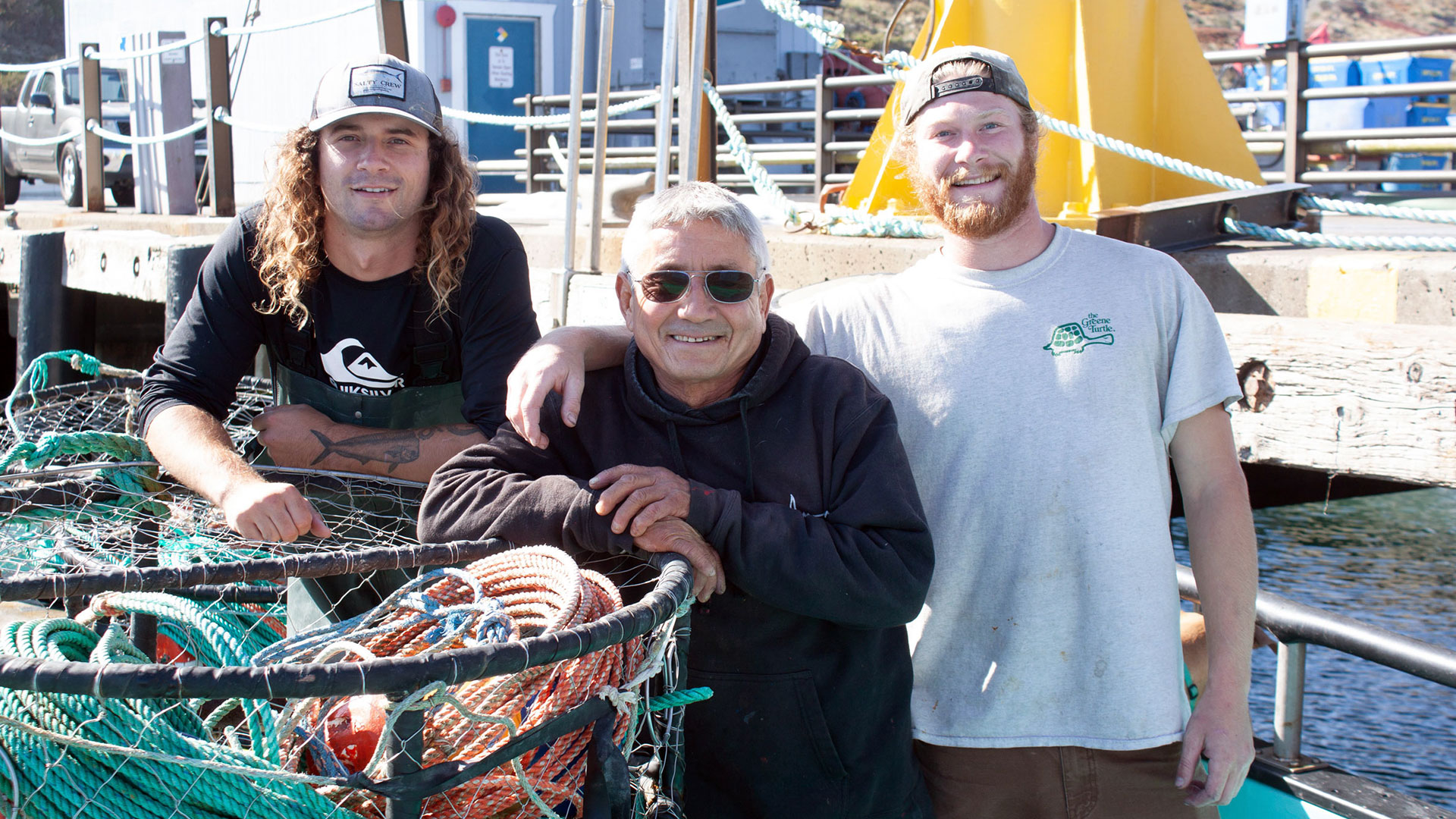 Three fisherman pose on a pier with their crab pots in the foreground.
