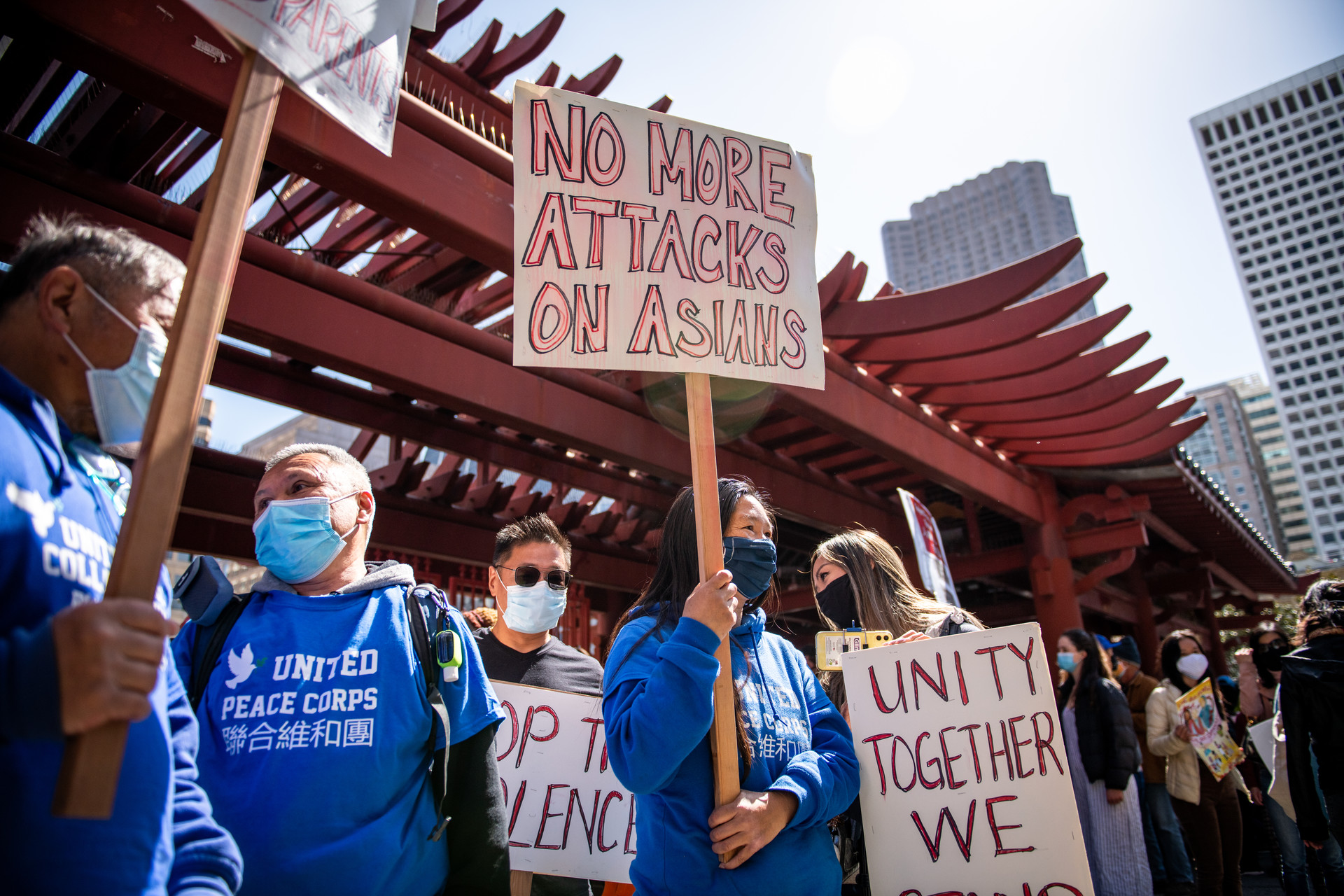 Four people wearing masks , with two people wearing blue t-shirts hold signs that read "no more attacks on Asians" and "Unity together."