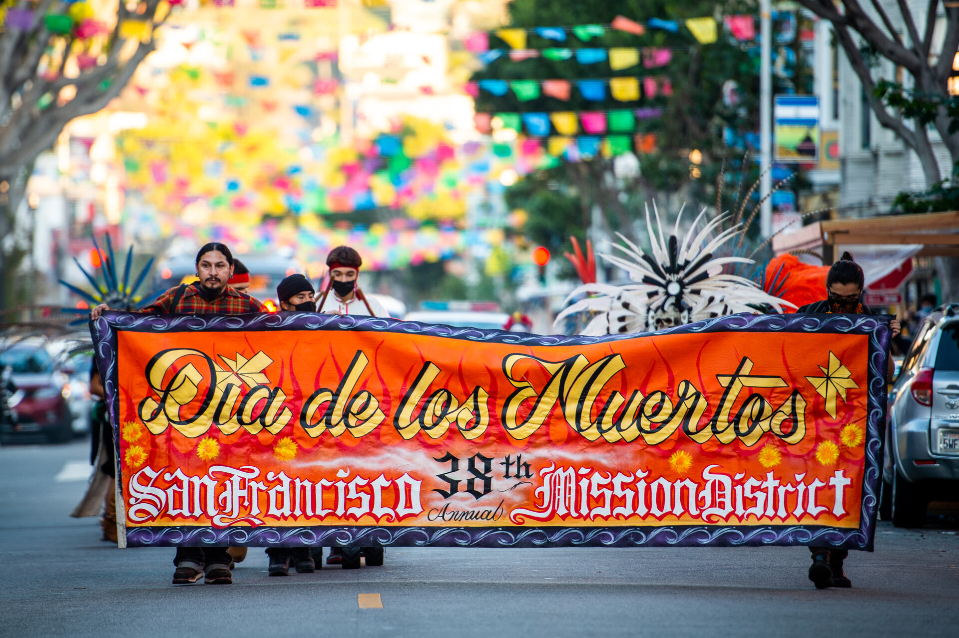 A group of people carries a bright orange banner down the middle of a street.