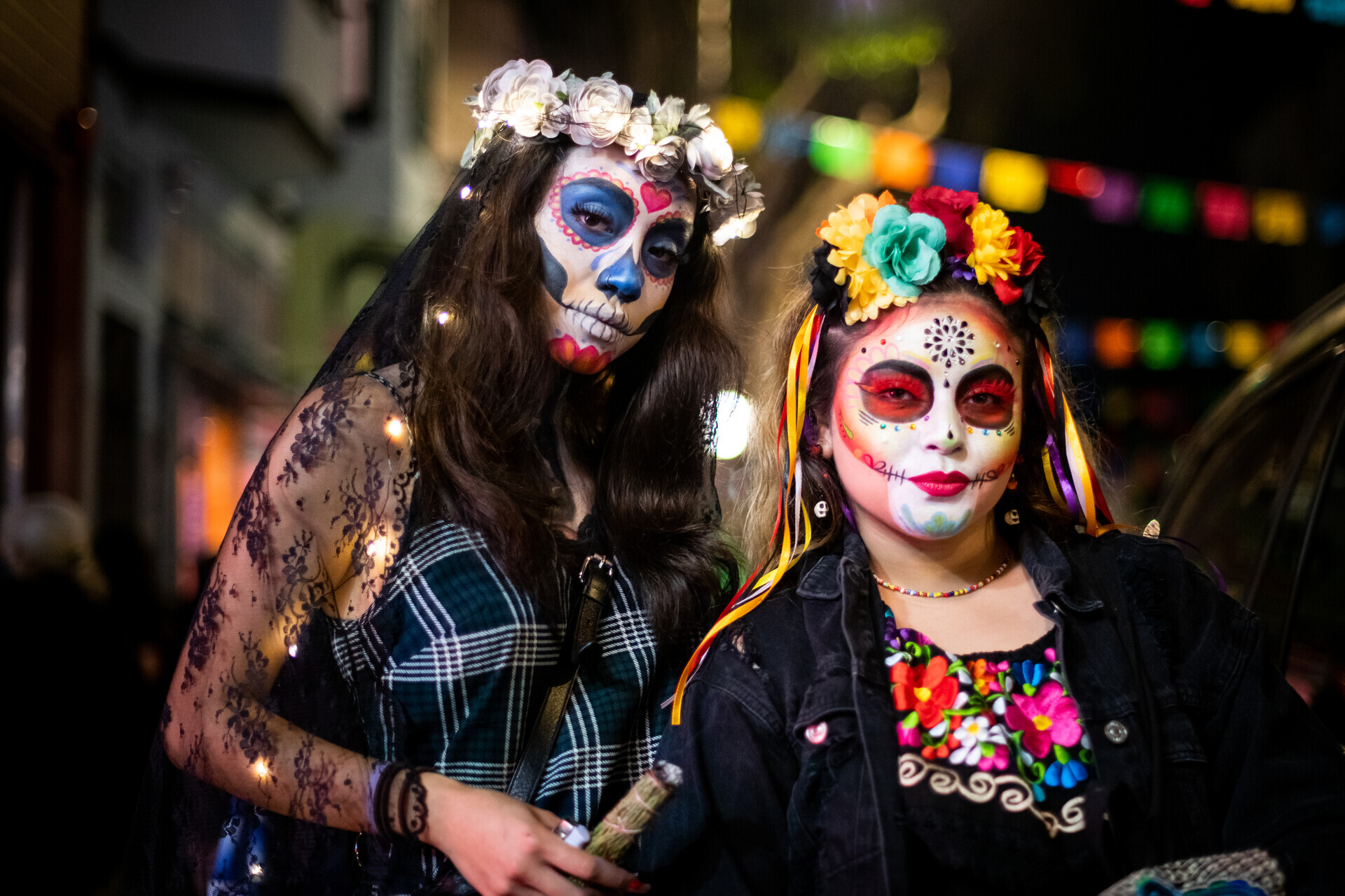 Two people wear face paint and flowers in their hair and look at the camera.