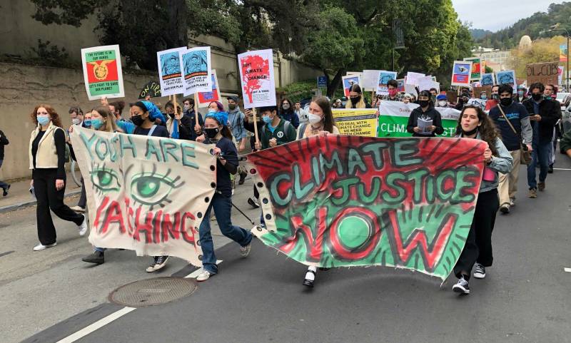 Young people walk down a street in Berkeley with small signs and big signs saying 'Climate Justice Now'.
